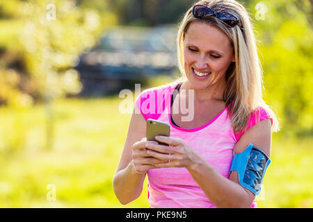 A young woman wearing active wear et un brassard de tenir son téléphone intelligent de textes avant de partir pour une course dans un parc de la ville pendant la saison d'automne Banque D'Images