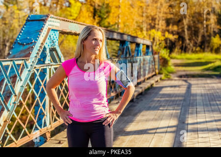 Une belle femme d'âge moyen s'arrête pour se reposer sur un pont au cours d'une analyse sur un beau soir chaud d'automne dans un parc de la ville ; Edmonton, Alberta, Canada Banque D'Images