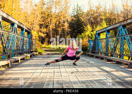 Une belle femme d'âge moyen s'arrête pour allonger ses jambes sur un pont au cours d'une analyse sur un beau soir chaud d'automne dans un parc de la ville Banque D'Images