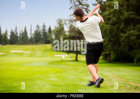 Un golfeur mâle au volant d'une balle de golf sur le green d'un terrain de golf avec la balle dans les airs ; Edmonton, Alberta, Canada Banque D'Images