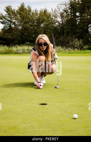 Un golfeur féminin s'accroupit vers le bas avec sa balle de golf et les lignes de son coup avant de faire une courte putt ; Edmonton, Alberta, Canada Banque D'Images