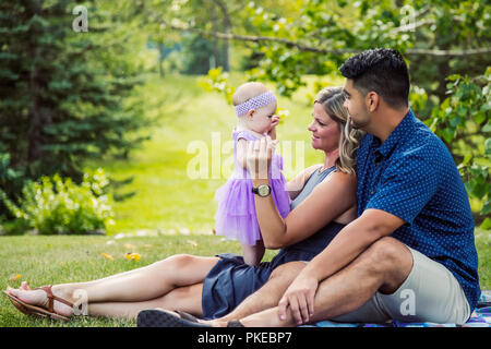 Une race mixte mari et femme se détendre ensemble avec leur petite fille sur une couverture dans un parc sur une chaude après-midi d'automne ; Edmonton, Alberta, Canada Banque D'Images