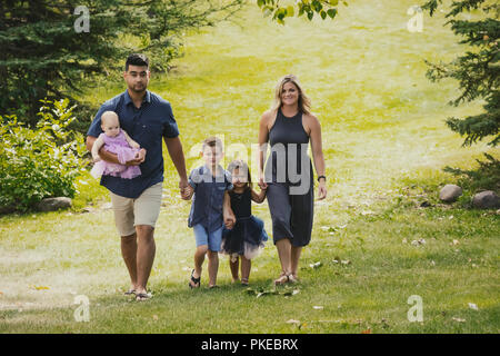 Une mère et un père dans un mariage de race mixte marchant avec leurs enfants dans un parc lors d'une sortie en famille pendant une chaude journée d'automne et leur fils pose pour... Banque D'Images