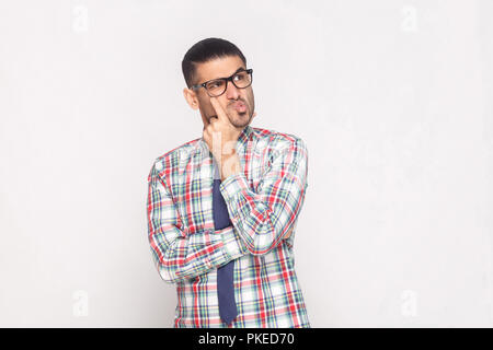 Portrait d'homme barbu beau confus en chemise à carreaux colorés, cravate bleue et lunettes l'article touchant le visage et à l'intérieur de l'hôtel. Banque D'Images