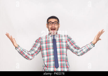 Surpris ou choqués de barbus chemise à carreaux, cravate bleue et lunettes debout, main levée et à la caméra avec surpris à ouvrir jsmn Banque D'Images