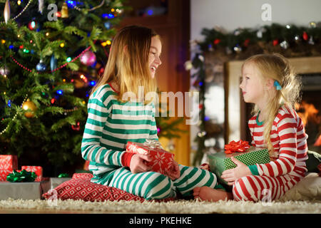 Happy Little Sisters wearing Christmas pyjama jouant par une cheminée dans un confortable salon sombre la veille de Noël. La célébration de Noël à la maison. Banque D'Images