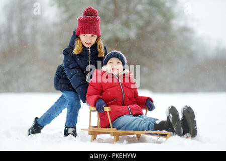 Deux petites filles s'amusant avec un traîneau dans le magnifique parc d'hiver. Mignon enfants jouant dans la neige. Activités d'hiver pour les enfants. Banque D'Images