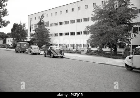 Années 1950, historiques, post -la guerre, l'image montre l'extérieur d'un grand bâtiment moderne, peut-être un hôtel et d'un van volkswagen et deux voitures garées dans une rue pavée à Cologne, Allemagne. Banque D'Images