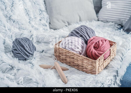 Boules de fil de laine merino chunky super avec des aiguilles dans le panier rustique sur fond de fourrure blanche pelucheuse. Banque D'Images