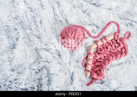 Rose de tricot chunky super fils de laine avec des aiguilles de bois blanches sur fond de fourrure, vue du dessus Banque D'Images