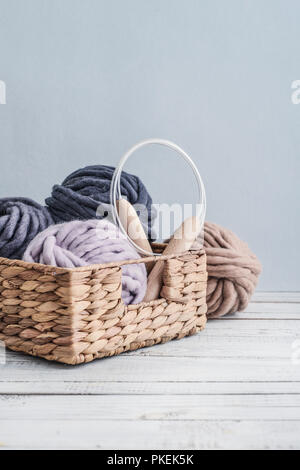 Boules de fil de laine merino chunky super avec des aiguilles dans le panier rustique sur fond bleu clair. Banque D'Images