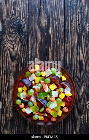 Délicieuse salade de fruits aux figues, framboises, raisin, mangue sur une plaque d'argile sur une table en bois rustique, vertical Vue de dessus Banque D'Images