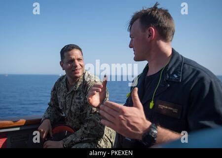 Mer rouge (1 août 2018) Le capitaine de vaisseau américain Adan Cruz, gauche, commodore du 5e flotte américaine Task Force 55, parle avec le lieutenant J.G. Nicholas Doeller sur l'aileron de passerelle de l'USS destroyer lance-missiles Jason Dunham (DDG 109) pendant l'exercice Eagle Salute 18. Salut Eagle 18 est un exercice avec l'ENF menée pour améliorer l'interopérabilité et l'état de préparation au combat, fortifier les relations militaires et de faire progresser les capacités opérationnelles de l'ensemble des unités participantes. Jason Dunham est déployé sur le 5e flotte américaine zone d'opérations à l'appui des opérations navales pour assurer stabilité et maritime Banque D'Images