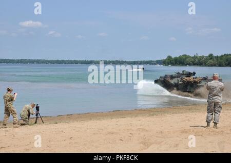 Le Sgt. Brandon Burk, un sous-officier des affaires publiques avec la 135e Détachement des affaires Public Mobile, de l'Iowa Army National Guard casseroles sa caméra comme Marines entrer Lake Margrethe avec leurs véhicules d'assaut amphibie à Camp Grayling, Michigan, le 8 août 2018. Une compagnie de marines, 4e, 4e Bataillon d'assaut amphibie Marine Division, U.S. Marine Corps de réserve des Forces canadiennes, à Norfolk, Virginie participent à Northern Strike, un projet conjoint interarmes multinationales exercice de tir réel. Banque D'Images