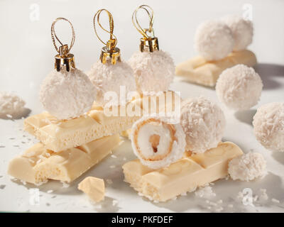 Petit rond jaune pâle en copeaux de noix de coco bonbons sous la forme de jouets de Noël avec des bouchons d'or sur les barres de chocolat blanc Banque D'Images