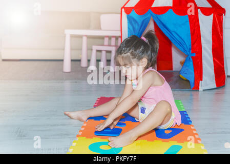 Vue latérale d'une mignonne petite fille est assise et tapis de jeu de puzzle coloré tient avec des nombres à la maison. Banque D'Images
