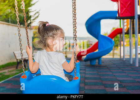 Vue arrière d'un cute little girl holding chaises et se balançant sur l'aire de jeux Banque D'Images