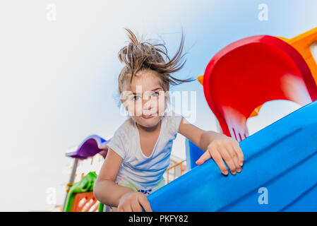 Portrait of cute little girl holding et de l'escalade pour atteindre les curseurs haut sur jeux pour enfants Banque D'Images