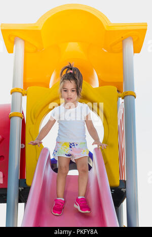 Portrait of cute little girl essayant de marcher sur glissière rose de haut en bas sur l'aire de jeux Banque D'Images