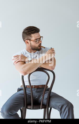 Beau barbu son cigare d'éclairage tout en étant assis sur une chaise isolé sur fond blanc Banque D'Images