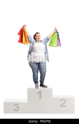 Portrait d'une très grande joie woman with shopping bags debout sur un piédestal gagnants isolé sur fond blanc Banque D'Images