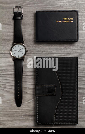Watch avec un bracelet en cuir, ordinateur portable en cuir, porte-carte nom sur un fond de bois gris Banque D'Images