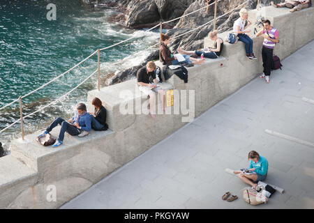 CINQUE TERRE, ITALIE - 25 avril 2011 ; les jeunes adultes voyageurs par mer de détente assis autour de plans de contrôle, l'écriture des lettres et journaux intimes ou relaxim Banque D'Images