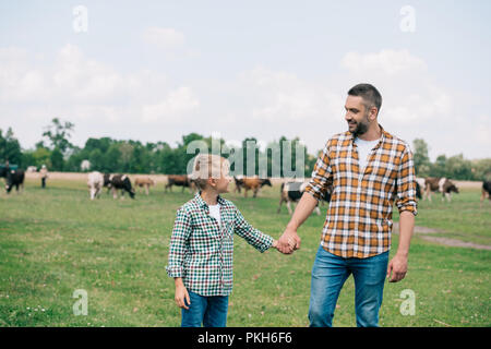 Heureux père et fils se tenant la main et en souriant les uns les autres à la ferme Banque D'Images