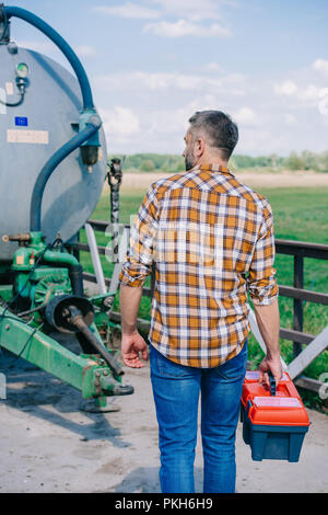 Vue arrière de l'agriculteur détenant d'âge moyen et à la boîte à outils à agricole véhicule Banque D'Images