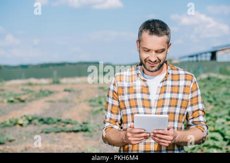 Handsome smiling farmer using digital tablet en se tenant sur le terrain Banque D'Images