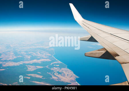 White aile d'avion. Vue aérienne de la surface de la mer bleue, la mer, les champs de la côte déchiquetée, ciel et l'horizon. Billet d'air le long d'une journée sans nuages Banque D'Images