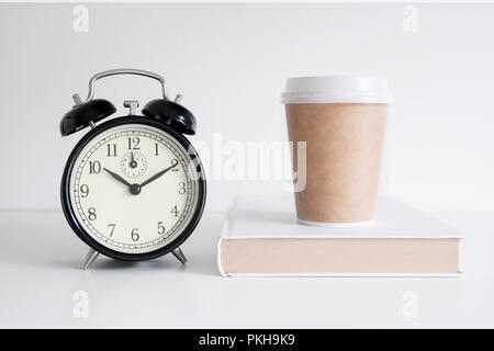 Réveil à côté d'un livre et une tasse de café sur une table en bois. Fond blanc et copie vide de l'espace pour l'éditeur de texte. Banque D'Images
