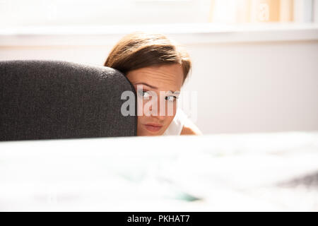 Peur Businesswoman Peeking du bord de Desk In Office Banque D'Images