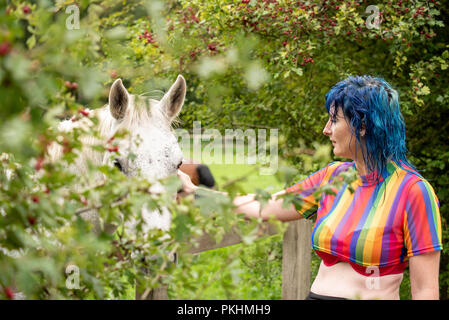 Une femme aux cheveux bleus coups un cheval blanc dans un pâturage Banque D'Images