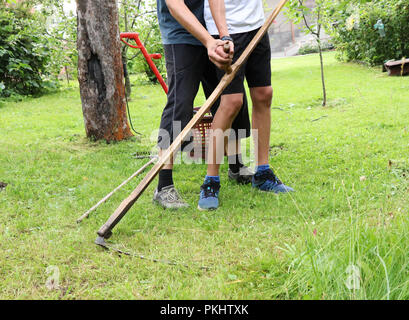 Un homme avec de l'herbe de tonte propre kid sur l'ancien chemin. Un père de l'enfant apprendre l'herbe de tonte avec faux. La vie du village Banque D'Images