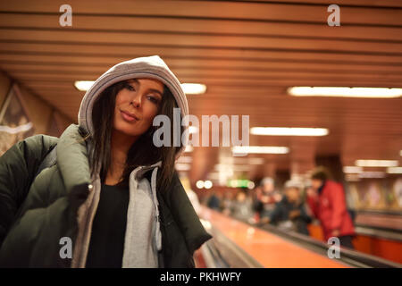 Portrait d'une belle jeune femme heureuse dans un manteau noir alors qu'il se trouvait sur un escalator d'une station de métro. Banque D'Images