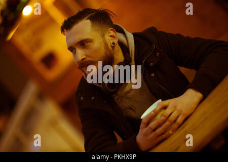 Un beau jeune hipster homme assis à la table et boire du vin dans la nuit dans un environnement urbain. Banque D'Images