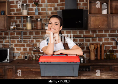 Smiling young repairwoman s'appuyant sur la boîte à outils et looking at camera Banque D'Images