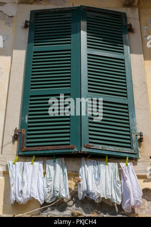Paires de pantalons et culottes grand accroché à un lave-ligne au-dessous de certains volets wodden peint en vert et une fenêtre dans la vieille ville de kerkyra sur Corfou. Banque D'Images