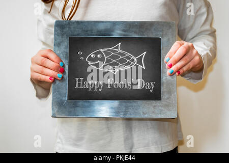 Young Girl holding up blackboard with happy Fools Day et le poisson Banque D'Images