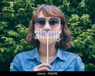 Belle asiatique femme cheveux courts porter un jean bleu shirt et lunettes avec fake moustache sur fond vert. Banque D'Images