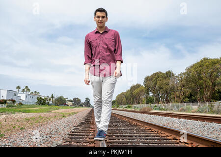 Jeune homme qui marche sur des rails de chemin de fer Banque D'Images