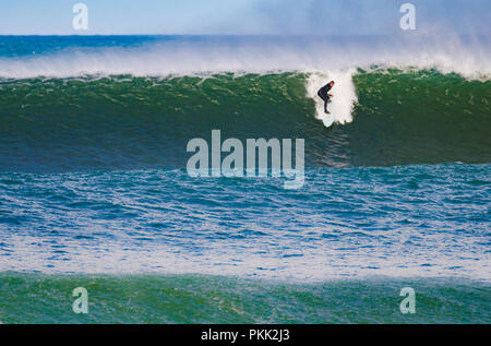 Un surfeur chevauche une grande vague verte en pleine mer, démontrant son habileté et son équilibre sur la planche de surf Banque D'Images
