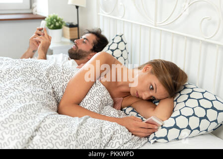 Jeune couple avec les smartphones dans leur lit. Mauvaise relation concept Banque D'Images