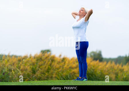 Le calme des profils woman wearing white tee shirt et pantalon bleu foncé avec les bras derrière la tête debout sur une grande pelouse verte Banque D'Images