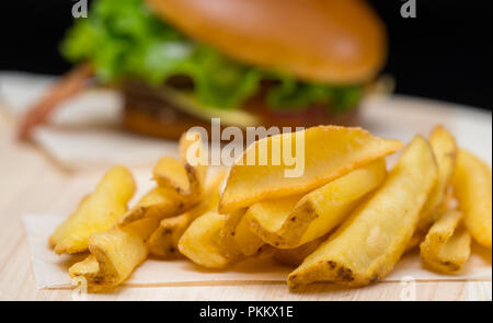 Or croustillant chips de pomme de terre frite ou frites servies avec un hamburger sur une planche en bois, vue en gros Banque D'Images