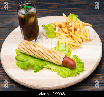 Vue de dessus de hot dog fourré dans du pain et des tas de frites à côté de verre de soude avec de la glace assis sur plateau en bois blanc Banque D'Images