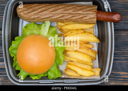 Vue aérienne sur noir contenant de burger assis à côté de tranches de pommes de terre et la chair à saucisses enveloppées dans du pain Banque D'Images