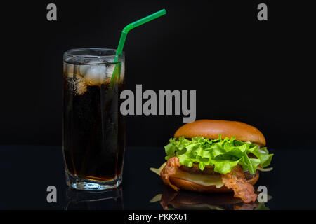 Bacon burger rempli de feuilles de laitue et grand verre de soda contenant de la glace assis sur table réfléchissant Banque D'Images