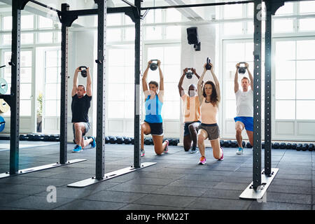 Groupe diversifié de jeunes faisant se jette avec les poids dans une salle de gym ensemble lors d'un entraînement Banque D'Images